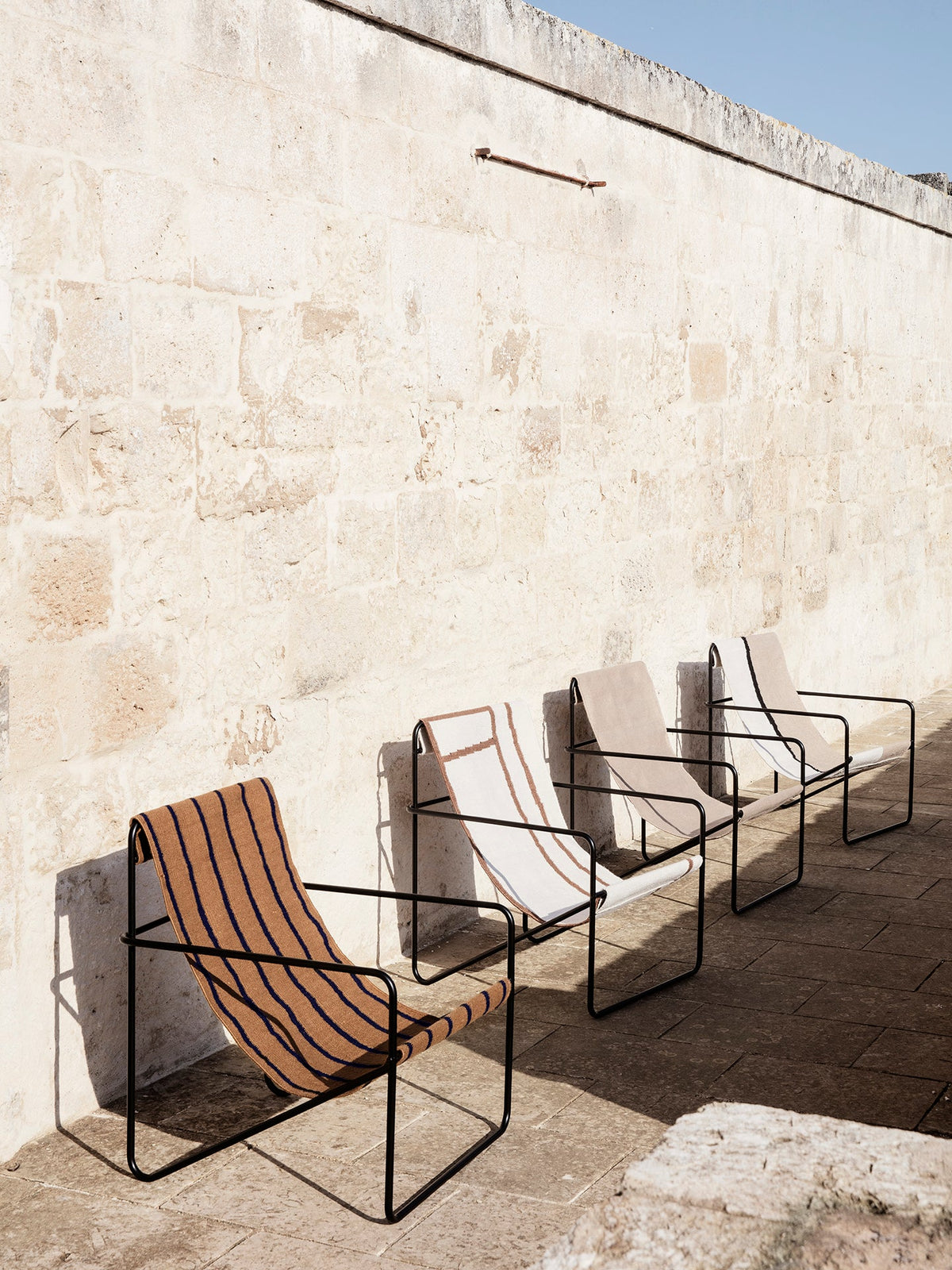 Fauteuil Desert - Ferm Living-Black - Soil, en situation contre un mur de pierre-The Woods Gallery
