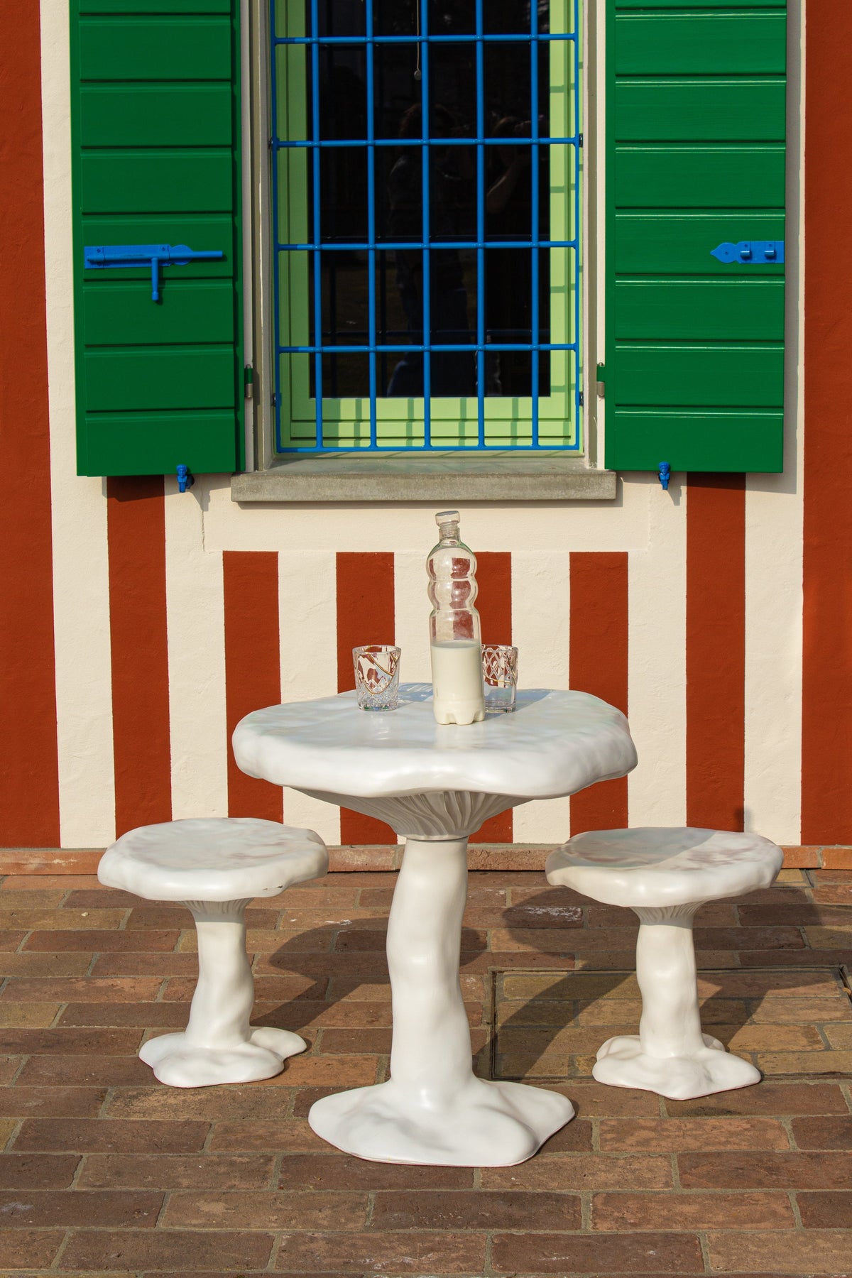 Table Amanita blanche de Marcantonio - Seletti-table et tabourets blancs devant une façade rayée à volets verts-Seletti