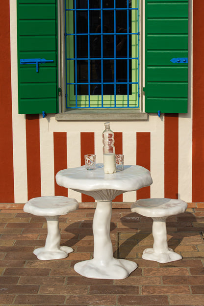 Table Amanita blanche de Marcantonio - Seletti-table et tabourets blancs devant une façade rayée à volets verts-Seletti