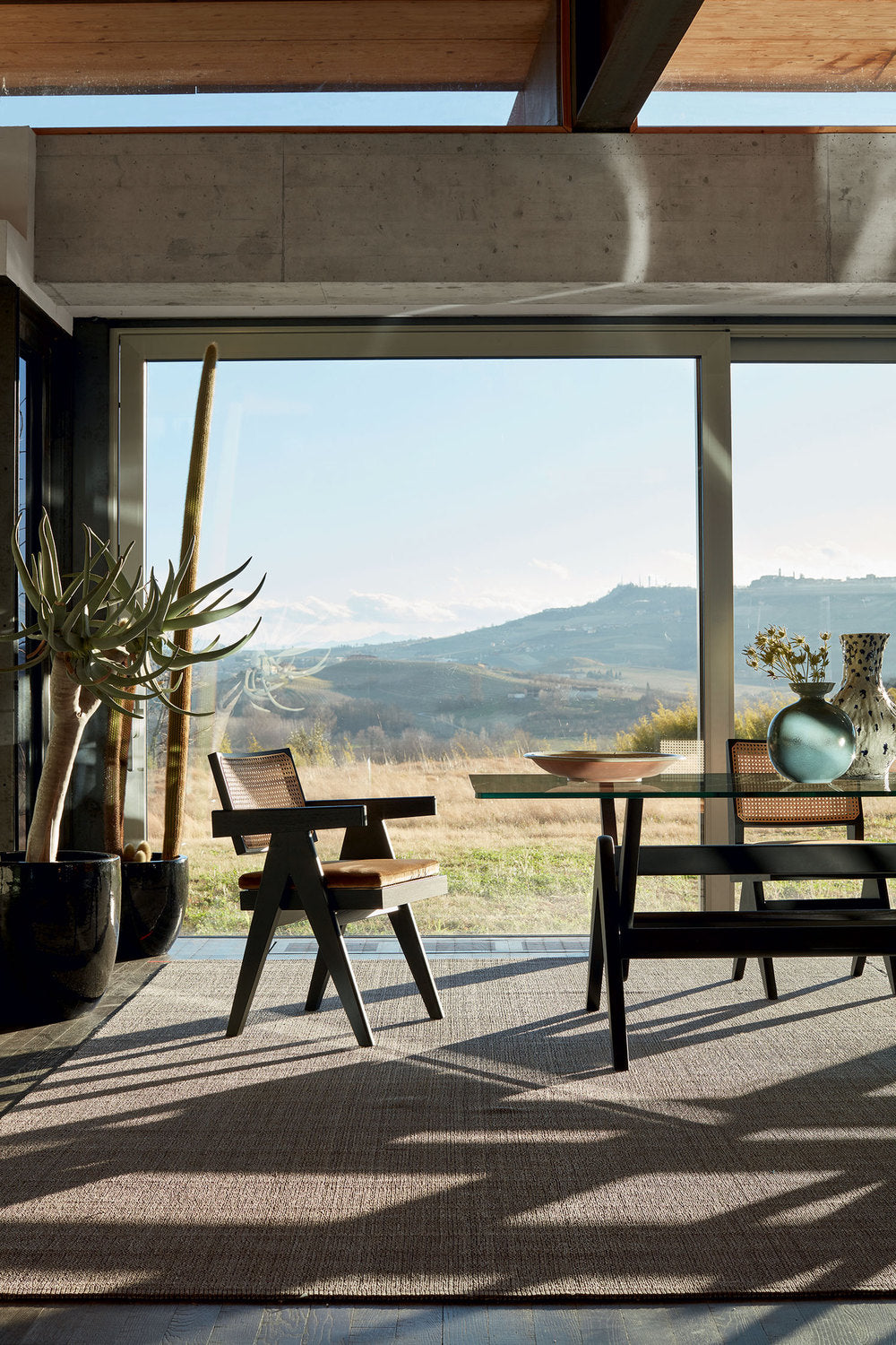 Table 056 Capitol Complex de Pierre Jeanneret - Cassina-fauteuil et banc noirs devant une baie sur les collines-Cassina