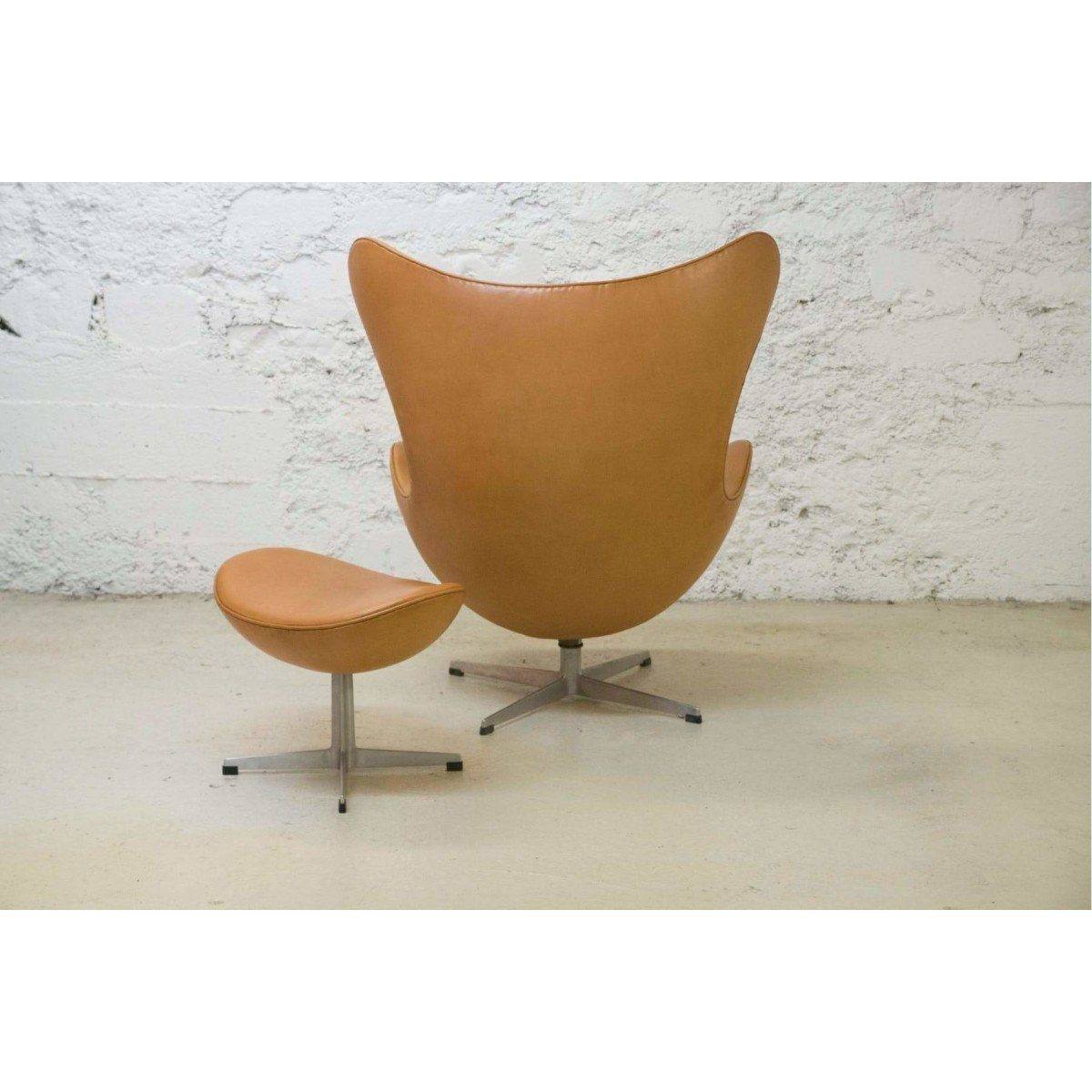 Fauteuil pivotant Egg Chair et son ottoman d'Arne Jacobsen pour Fritz Hansen, cuir cognac, devant un mur de briques peint en blanc