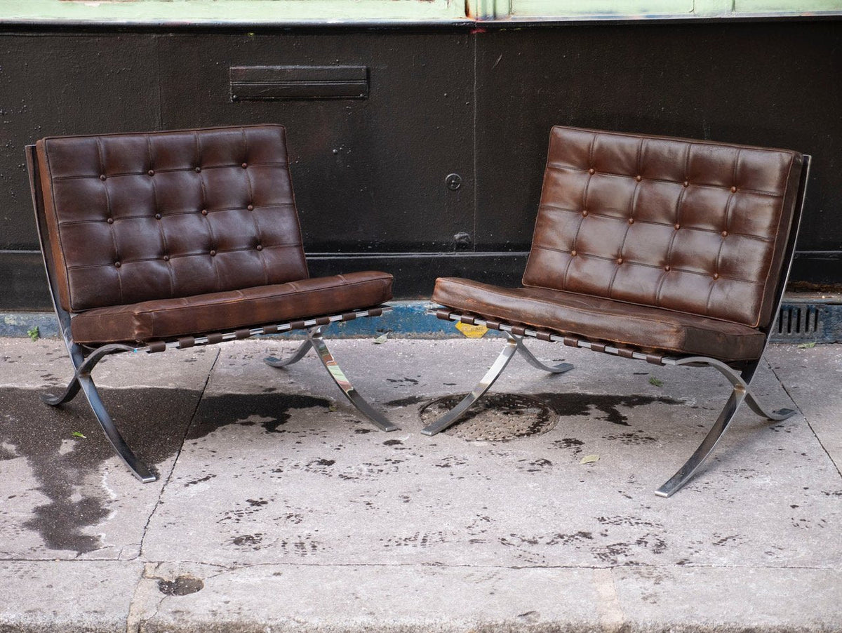 Paire de fauteuils Barcelona de Mies van der Rohe pour Knoll, cuir brun patiné et piètement chromé, posés devant une façade noire